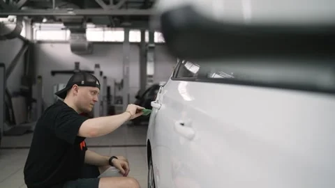 Professional car wrapper applying vinyl wrap on vehicle door handle Stock Footage 306128964