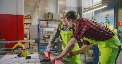 Professional carpenter teaching female apprentice how to cut wood using handsaw Stock Footage 112063397