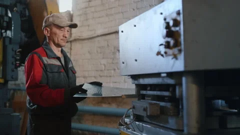 A professional Caucasian engineer in overalls processes a sheet of metal on a Stock Footage 137535234