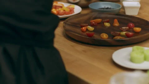 Professional chef assembling sliced tomatoes onto a wooden plate for serving in Stock Footage 199455745
