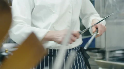 Professional chef in a commercial kitchen in a restaurant is sharpening knifes Stock Footage
