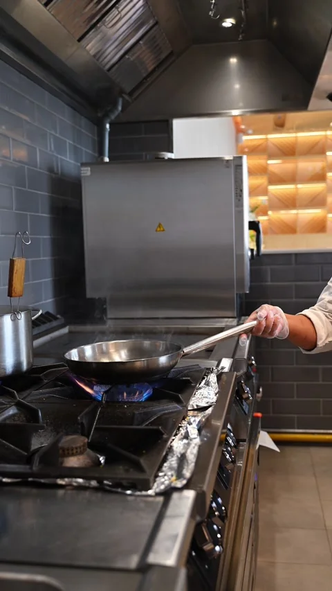 Professional chef cooking with a frying pan over a blue gas flame burner on.. Stock Footage 338053673