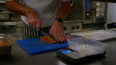 Professional chef cuts up fish as he prepares food in a professional kitchen Stockbeeldmateriaal 289446188