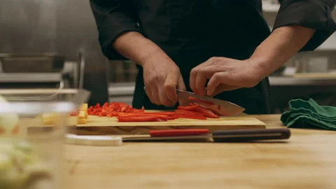 Professional chef cutting red pepper into thin pieces on a cutting board in indu Stock Footage 199459480