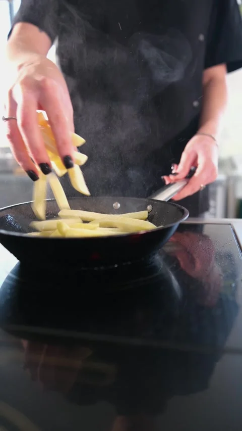 Professional chef drops raw potato sticks into a hot frying pan on an electric Video stock 318316375
