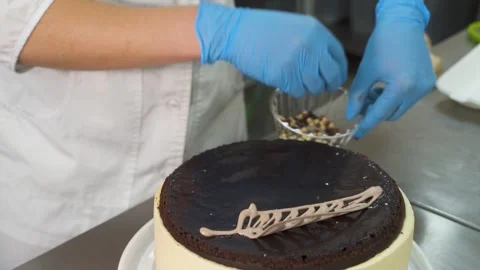A professional chef in gloves decorates a cream cake with decorations and nuts Video stock 263039341