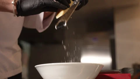 Professional chef grating hard cheese into a white bowl in a restaurant kitchen Stock Footage 338392847