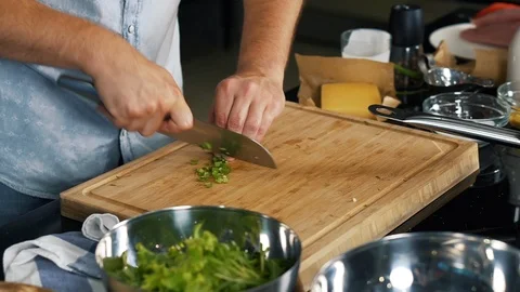 Professional chef near kitchen table, expertly slices green seasoning with knife Stock Footage 122903168