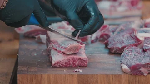 Professional chef or butcher preparing raw beef. Gloved hands use a sharp knife Stock Footage 345499706