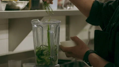 Professional chef placing herbs into a blender with cucumber in industrial kitch Stock Footage 199460629