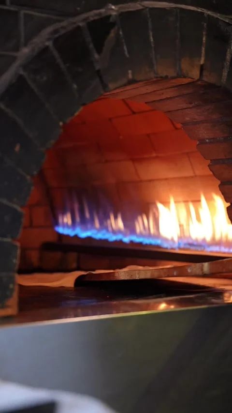 Professional chef placing pizza dough into hot wood fired oven with flames. Stock Footage 337783842