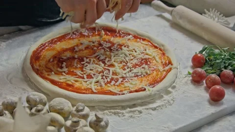 Professional chef pours grated cheese onto a pizza base with tomato paste on the Stock Footage 153036775