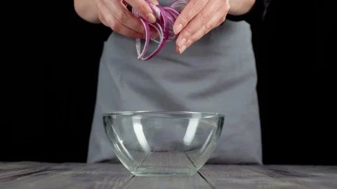 Professional chef pours sliced purple onion in empty glass bowl on wooden table Stock Footage 129745775