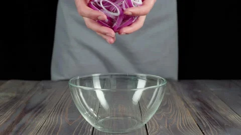 Professional chef pours sliced purple onion in empty glass bowl on wooden table Stock Footage 130516054