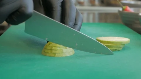 A professional chef quickly cuts eggplants on a board using a knife. Close-up Stock Footage 96392592