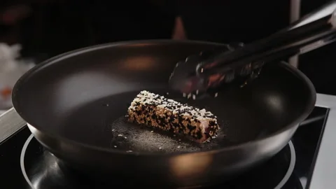 Professional chef roasts and rotate by with kitchen tongs tuna roll with sesame Stock Footage 153315006