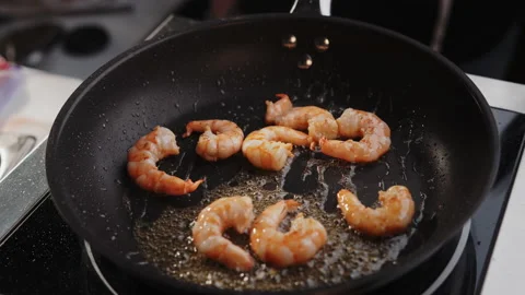 Professional chef roasts and tosses prawns in a black frying pan with olive oil Stock Footage 153314663
