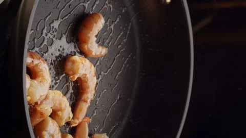 Professional chef roasts and tosses prawns in black frying pan with olive oil in Stock Footage 168445240