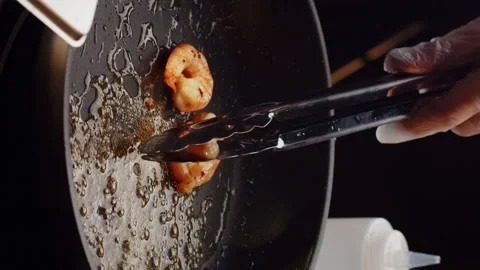 Professional chef roasts and tosses prawns in black frying pan with olive oil in Vídeo Stock 168445253