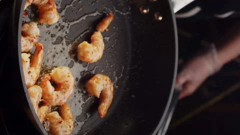 Professional chef roasts and tosses prawns in black frying pan with olive oil in Stock Footage 168473581
