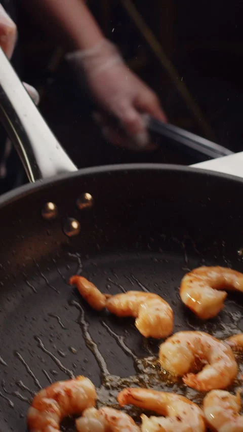 Professional chef roasts and tosses prawns in black frying pan with olive oil in Stock Footage 247005407