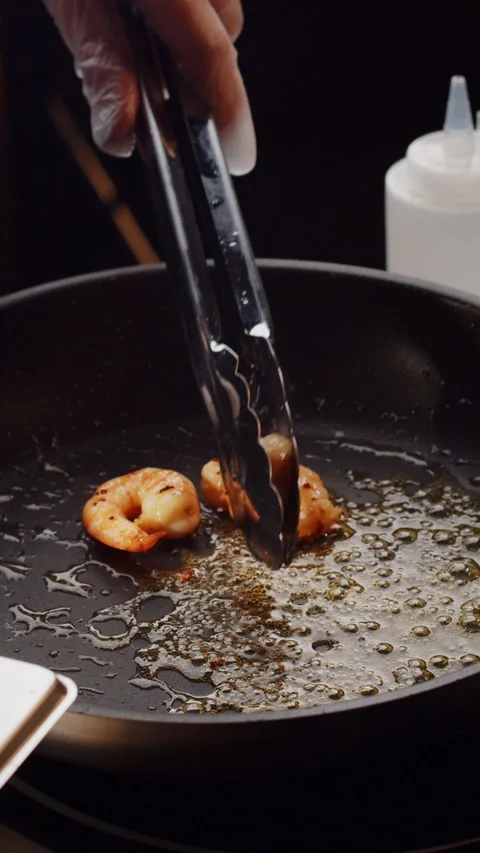 Professional chef roasts and tosses prawns in black frying pan with olive oil in Stock Footage 247005409
