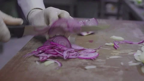 Professional chef slicing fresh red onions on wooden board in restaurant kitchen 스톡 동영상 332116472