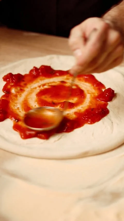 Professional chef spreading tomato sauce on pizza dough in bright kitchen. Stock Footage 346400435