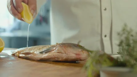 Professional Chef Squeezes Lemon Juice onto Fish on Wooden Board. Close-up. Stock Footage 196259617
