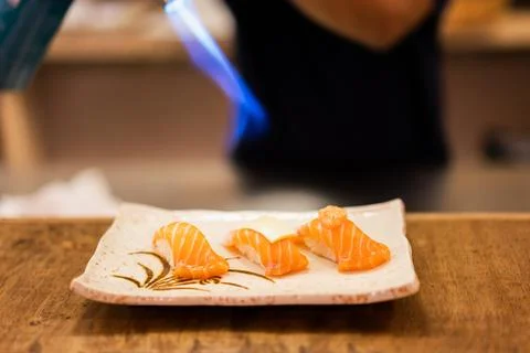 Professional Chef Using Blowtorch to Sear Fresh Salmon Sushi Nigiri on Plate Stock Photos