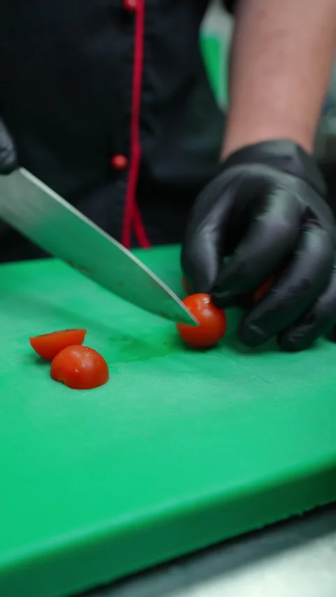 Professional chef wearing black gloves cutting fresh cherry tomatoes on green Stock Footage 309118877