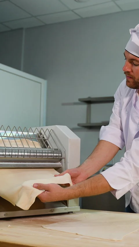 Professional chef in a white uniform placing a sheet of dough into a dough Stock Footage 299655027