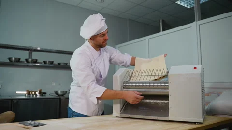 Professional chef in a white uniform placing a sheet of dough into a dough Stock Footage 299659036