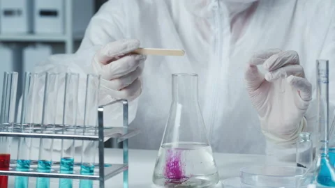 Professional chemist wearing protective uniform with gloves adding pink powder Stock Footage 156752818