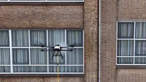 Professional cleaning drone washing windows of an old brick building Stock Footage 343462601
