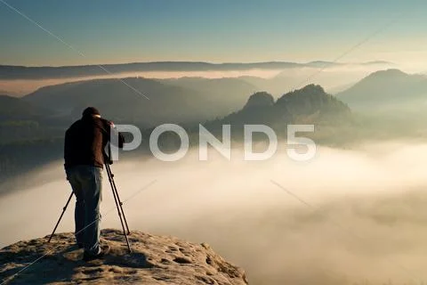 Professional on cliff. Nature photographer takes photos with mirror camera on Stock Photos