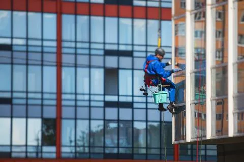 Professional climber rope access worker cleaning the windows on the high rise Fotos Stock