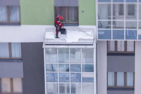 Professional climber rope access worker with a shovel removes snow and take o Stock Photos