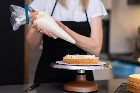Professional confectioner using pastry cone to put fresh cream on cake layers Stock Photos