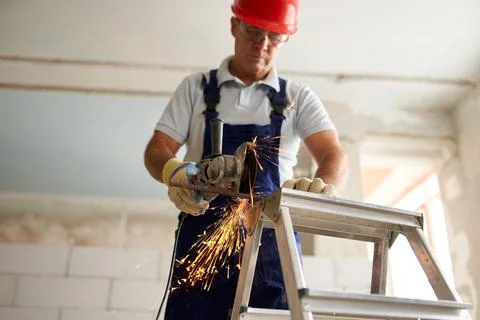 Professional construction worker hands in work gloves using angle grinder to cut Stock Photos