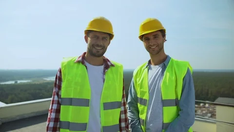 Professional construction workers in safety helmets and jackets smiling camera Vídeo Stock 117218855
