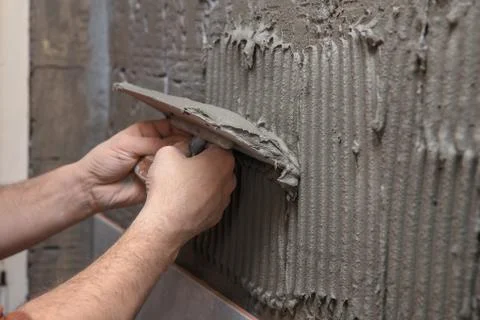 Professional constructor applying glue before laying ceramic tiles on the wall Фото