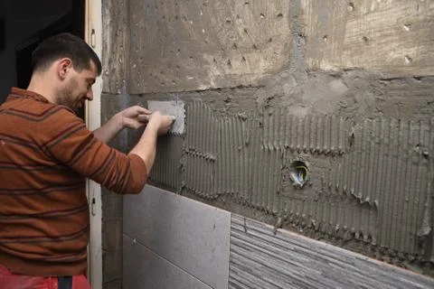 Professional constructor applying glue before laying ceramic tiles on the wall Photos