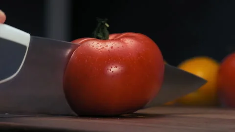 Professional cook cuts i half red tomato with steel knife 스톡 동영상 147029974