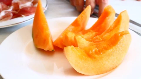 Professional cook cuts a slice of melon and prepares an appetizer with ham Stock Footage 76432110