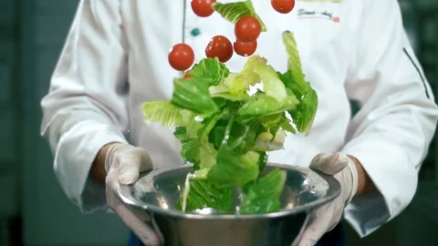 Professional cook in the kitchen throws up tomatoes and salad leaves Stock Footage 102654969