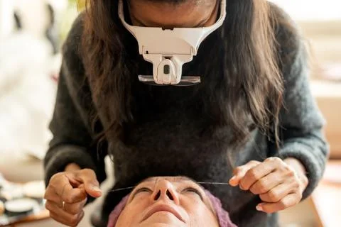 Professional cosmetologist plucking eyebrows with thread Stock Photos