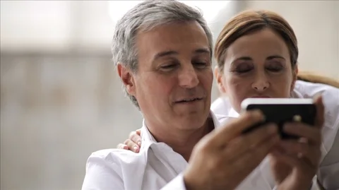 Professional couple affectionately looking at something on a cell phone. Vidéo 88342997