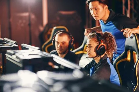 Professional cybersport team, two young guys and girl looking at PC screen Stock Photos