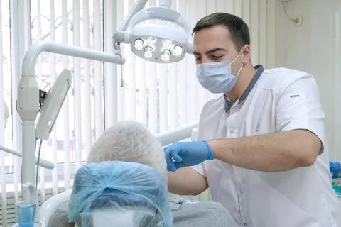 Professional dentist in protective mask working with elderly patient in dental Stock Photos